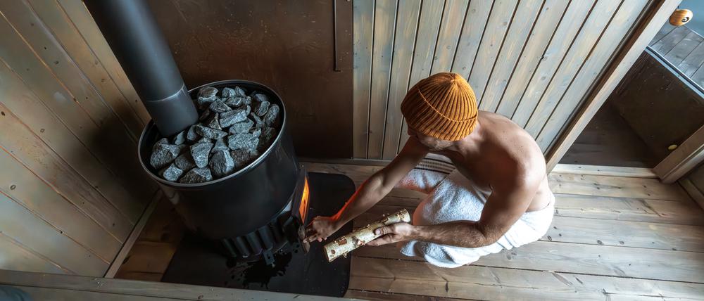 Ein junger Mann füllt den Saunaofen mit Holz auf. (Symbolbild)