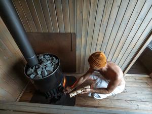 Ein junger Mann füllt den Saunaofen mit Holz auf. (Symbolbild)
