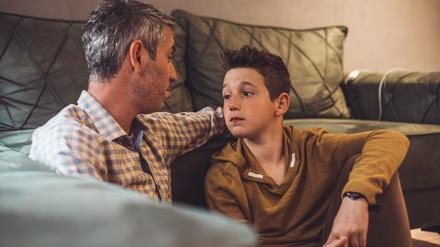 Ein Vater und sein Sohn sitzen vor einem Sofa auf dem Fußboden und führen ein ernsthaftes Gespräch.
