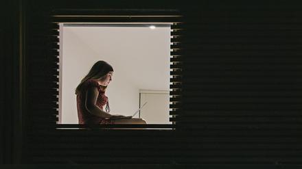 Eine Frau sitzt alleine an einem Fenster.
