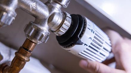 Eine Person dreht am Thermostat einer Heizung. 