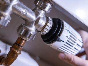 Eine Person dreht am Thermostat einer Heizung. 