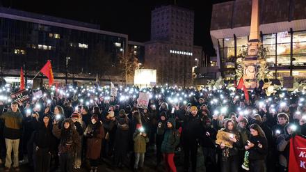 Zahlreiche Menschen versammeln sich bei einer Demonstration gegen die Migrationspolitik der CDU auf dem Augustusplatz und leuchten mit ihren Smartphones. 