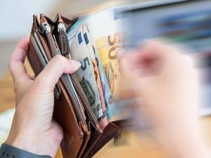 Eine Hand zieht einen 50-Euro-Schein aus einem Portemonnaie.