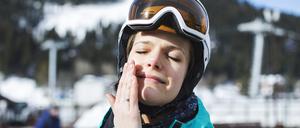 Eine junge Frau in Skikleidung hält ihr Gesicht in die Sonne und berührt mit ihrer Hand die Wange.