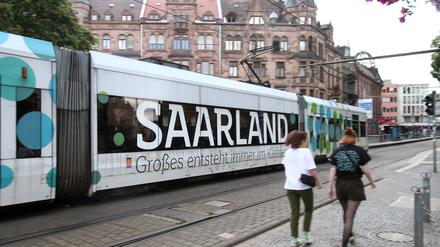 Eine Tram mit Werbeaufschrift „Saarland – Großes entsteht immer im Kleinen“ fährt vor dem Rathaus in der Innenstadt von Saarbrücken.