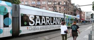 Eine Tram mit Werbeaufschrift „Saarland – Großes entsteht immer im Kleinen“ fährt vor dem Rathaus in der Innenstadt von Saarbrücken.
