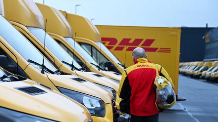Ein Paketbote von DHL geht zu seinem Elektrofahrzeug (Symbolbild).