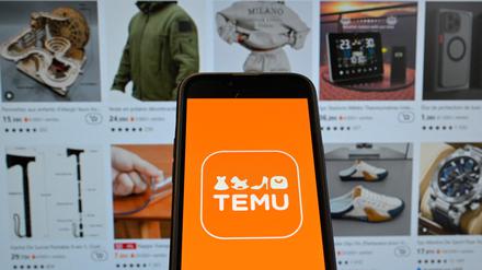 Das Logo von Temu auf einem Mobiltelefon mit der Website im Hintergrund.