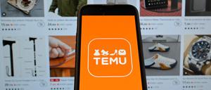Das Logo von Temu auf einem Mobiltelefon mit der Website im Hintergrund.