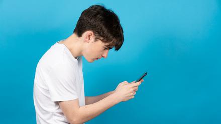Ein Teenager starrt mit gebeugtem Rücken auf ein Smartphone. 