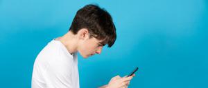Ein Teenager starrt mit gebeugtem Rücken auf ein Smartphone. 