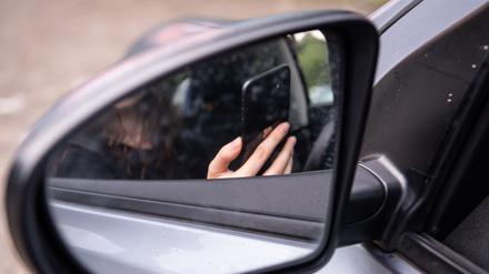 Eine Frau sitzt mit Handy am Steuer eines Autos.