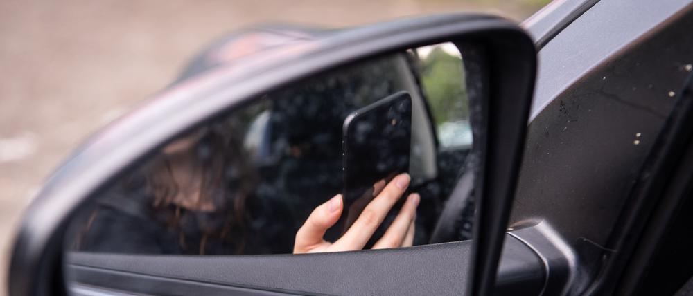 Eine Frau sitzt mit Handy am Steuer eines Autos.