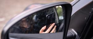 Eine Frau sitzt mit Handy am Steuer eines Autos.