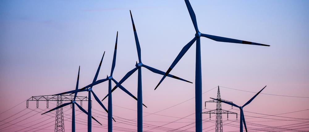 Windkraftanlagen und Hochspannungsleitungen sind vor dem Abendhimmel bei Leuna zu sehen.