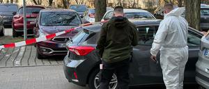 Zwei Beamte der Spurensicherung stehen vor einem Auto, das mit Absperrband gesichert ist. Mit lebensgefährlichen Verletzungen ist ein Paar in seiner Wohnung in Berlin-Marzahn gefunden worden. Für den Mann kam jede Hilfe zu spät, wie die Polizei mitteilte