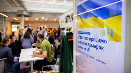 Menschen unterhalten sich bei einer Jobmesse für ukrainische Geflüchtete von der IHK Berlin und der Agentur für Arbeit an einem Infostand (Symbolbild).