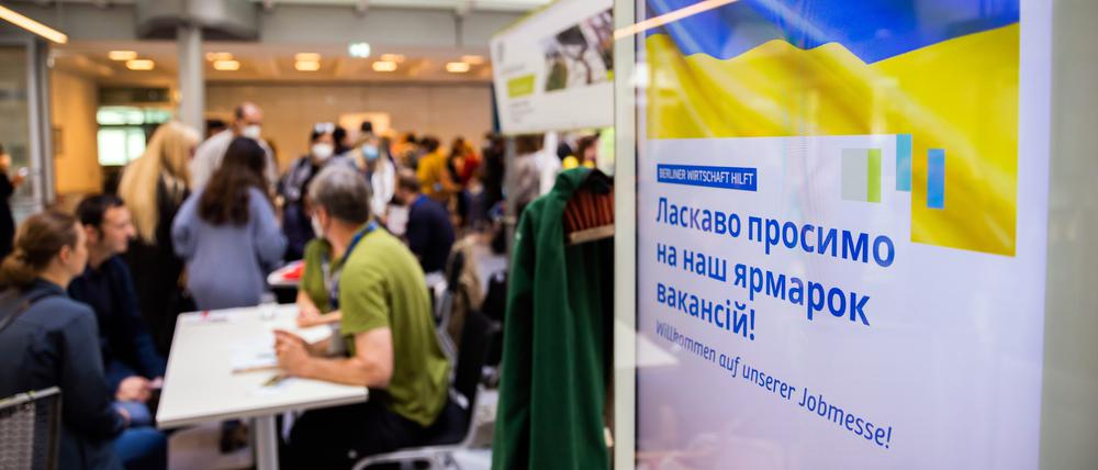 Menschen unterhalten sich bei einer Jobmesse für ukrainische Geflüchtete von der IHK Berlin und der Agentur für Arbeit an einem Infostand (Symbolbild).