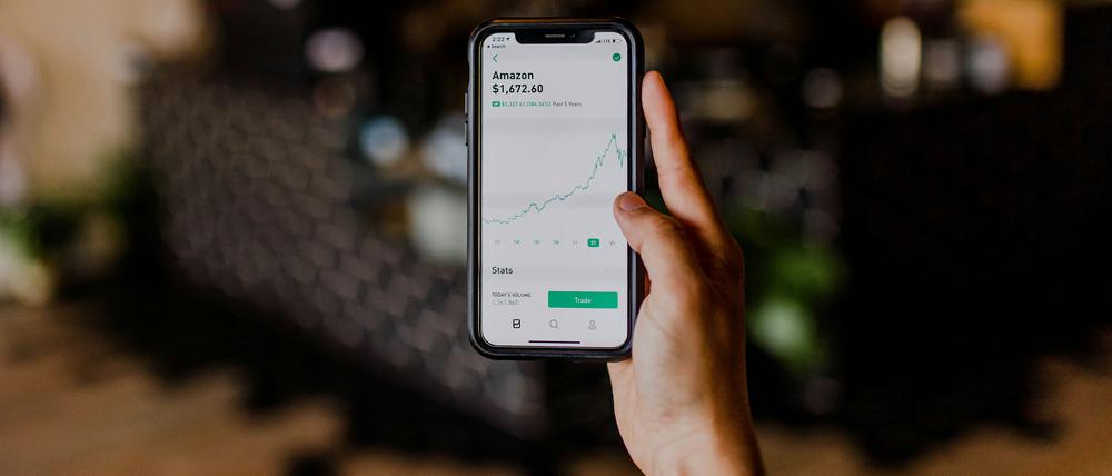 Eine Hand hält ein Smartphone, auf dem ein einbrechender Amazon-Chart zu sehen ist.