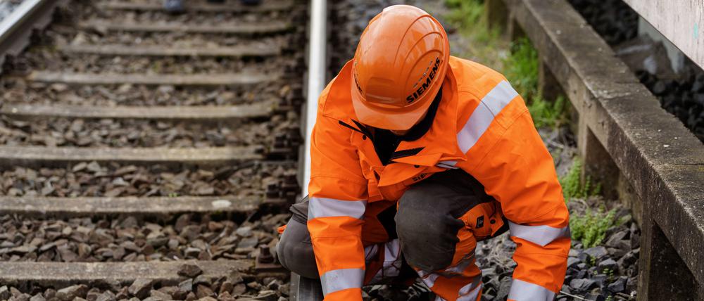 Ein Siemens-Mitarbeiter zeigt wie eine Balise, technische Einrichtung zum Übertragen von Informationen an das Schienenfahrzeug, im Gleis montiert wird.