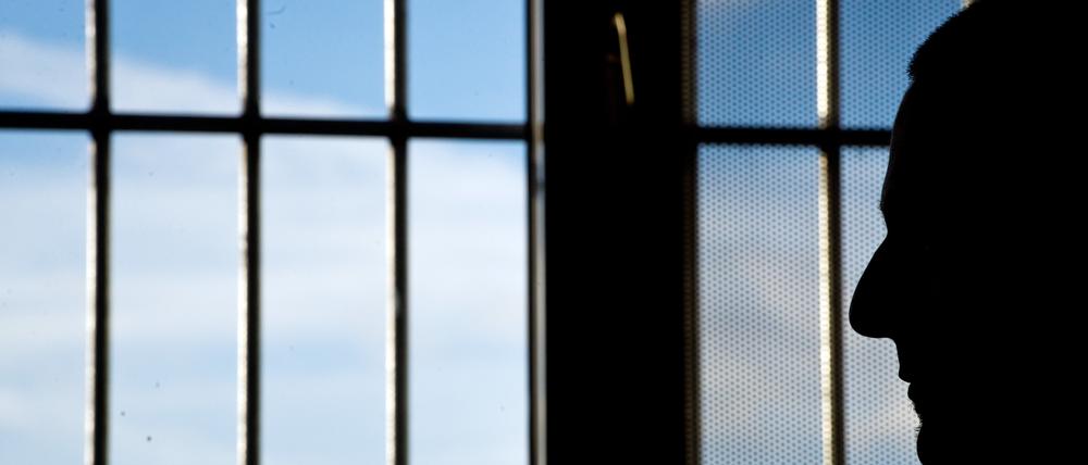 Ein Gefängnisinsasse sitzt in einer Justizvollzugsanstalt vor einem vergitterten Fenster.