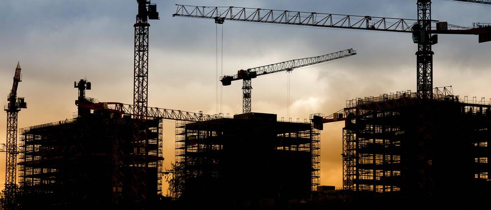 Silhouetten von Kränen auf einer Baustelle mit Rohbauten.