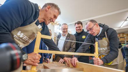 Friedrich Merz (r), Unions-Kanzlerkandidat und CDU-Bundesvorsitzender, sägt neben Schauspieler Ralf Moeller (l) und Handwerkspräsident Jörg Dittrich (2.v.l.) beim Betriebsbesuch der Wehner Tischlerei für die Initiative Motivation Handwerk während seiner Wahlkampftour.