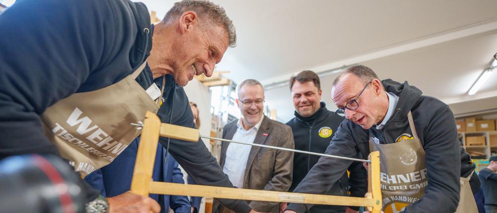 Friedrich Merz (r), Unions-Kanzlerkandidat und CDU-Bundesvorsitzender, sägt neben Schauspieler Ralf Moeller (l) und Handwerkspräsident Jörg Dittrich (2.v.l.) beim Betriebsbesuch der Wehner Tischlerei für die Initiative Motivation Handwerk während seiner Wahlkampftour.