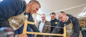 Friedrich Merz (r), Unions-Kanzlerkandidat und CDU-Bundesvorsitzender, sägt neben Schauspieler Ralf Moeller (l) und Handwerkspräsident Jörg Dittrich (2.v.l.) beim Betriebsbesuch der Wehner Tischlerei für die Initiative Motivation Handwerk während seiner Wahlkampftour.
