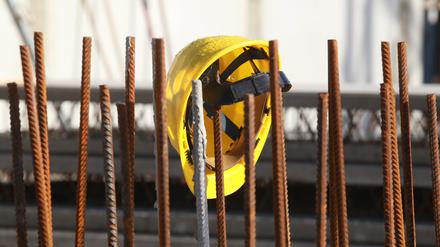 Ein Bauhelm hängt an Fundament-Stangen auf einer Baustelle (Symbolbild).