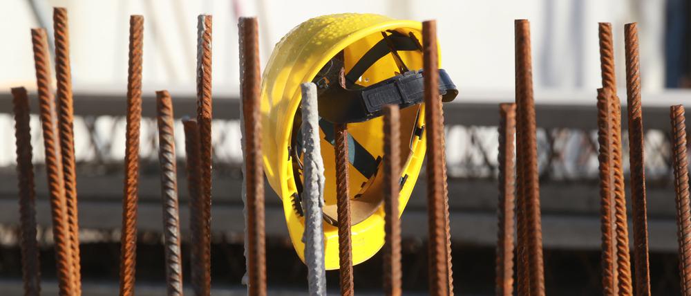 Ein Bauhelm hängt an Fundament-Stangen auf einer Baustelle. 