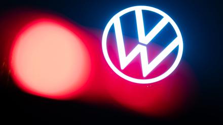 Eine rote Auto-Rückleuchte leuchtet am frühen Morgen vor dem Logo auf dem Dach des VW-Markenhochhauses. 