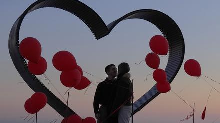 Ein Paar umarmt sich, während es vor einem mit roten Luftballons geschmückten Herz-Aussichtspunkt steht.
