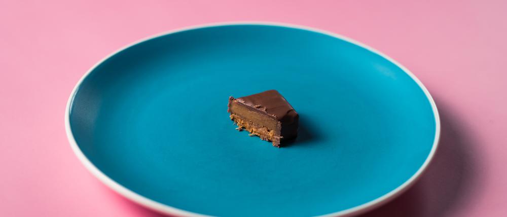 Uneaten slice sweet dessert chocolate bar on colored plate on pink background.
