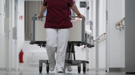 Eine Krankenpflegerin und ein Krankenpfleger schieben ein Krankenbett durch den Gang einer Station eines Krankenhauses.