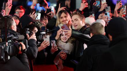 Der englische Schauspieler Robert Pattinson steht inmitten von Fans für Selfies bereit.  