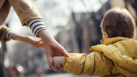 Ein Kleinkind läuft an der Hand der Mutter.
