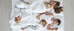 Mutter, Vater und zwei Kinder schlafen eng aneinandergedrückt auf einem schmalen Bett.
