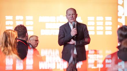 Bundeskanzler Olaf Scholz (M, SPD) spiegelt sich beim Wahlkampfabschluss in seinem Wahlkreis in einer Tischscheibe.