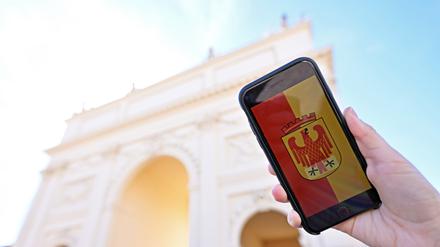 Ein Handy mit dem Potsdam-Wappen im Display wird vor das Brandenburger Tor in Potsdam gehalten.