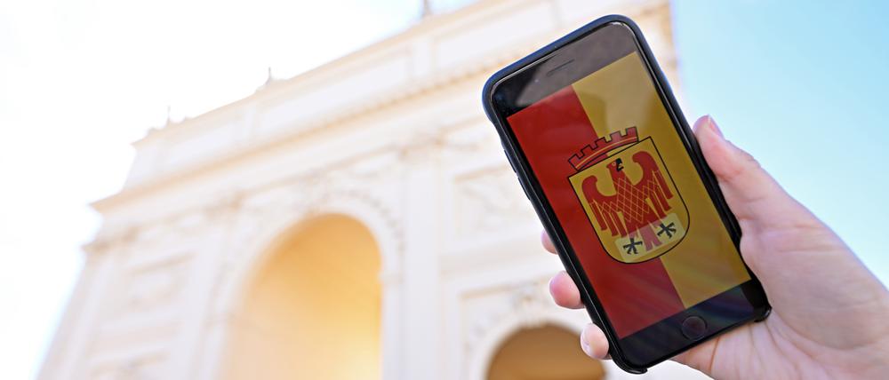 Ein Handy mit dem Potsdam-Wappen im Display wird vor das Brandenburger Tor in Potsdam gehalten.