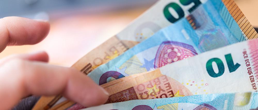 Eine Frau hält ein Portemonnaie in der Hand, in dem Geldscheine stecken.