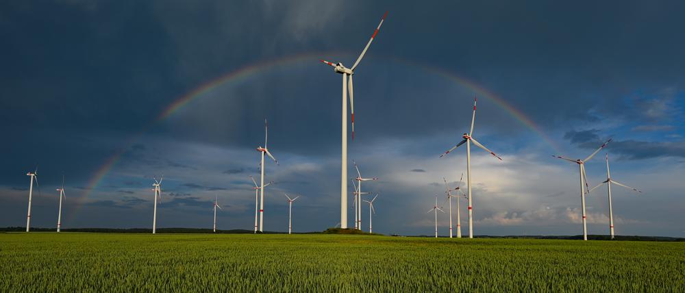 Ein Regenbogen ist vor dunklen Wolken am Abend über der Landschaft mit einem Windenergiepark im Osten von Brandenburg zu sehen.