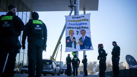 Polizeibeamte am Paul-Löbe-Haus neben dem Protestbanner eines Künstlerkollektivs, das gemalte Bilder von Alice Weidel, Kanzlerkandidatin und Fraktionsvorsitzende der AfD, und Friedrich Merz, Unions-Kanzlerkandidat und CDU-Bundesvorsitzender, zeigen soll. 