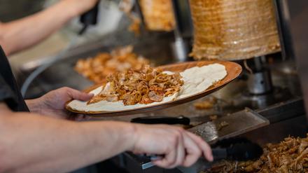 Ein Mitarbeiter einer Dönerbude legt Fleisch auf einen Döner.
