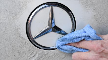 Eine Hand säubert an einem Mercedes-Benz Fahrzeug das Logo. 