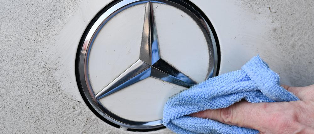 Eine Hand säubert an einem Mercedes-Benz Fahrzeug das Logo. 