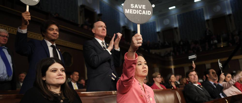 Die Abgeordnete Jill Tokuda hält mit ihren Demokratenkollegen ein Protestschild, als US-Präsident Donald Trump am 4. März 2025 in Washington, DC, vor einer gemeinsamen Sitzung des Kongresses im US-Kapitol spricht.