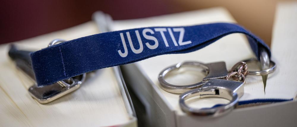 Handschellen und ein Bändel mit der Aufschrift „Justiz“ in Nahaufnahme. (Symbolbild)